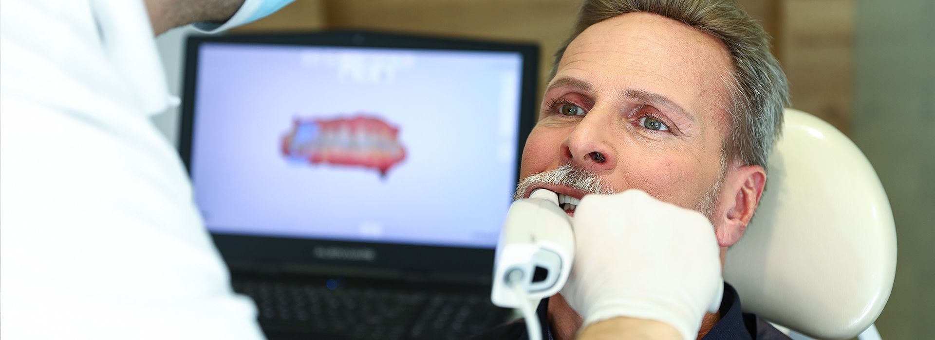 The image shows a man receiving dental treatment from a professional in a clinical setting.