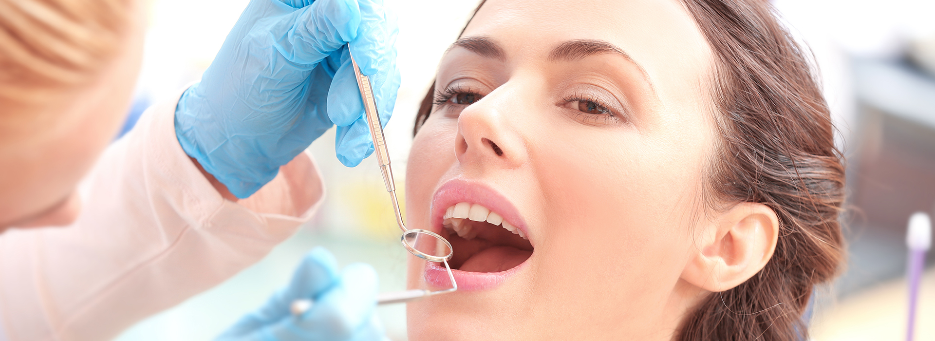 A woman receiving dental care with a dentist using a dental drill on her tooth.